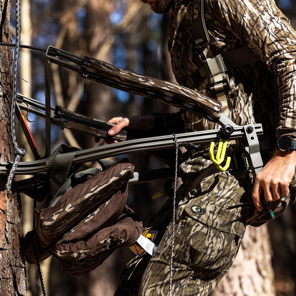 Man in camo ascends a tree using the Summit Dual Threat PRO SD climbing treestand. He is positioning the adjustable front bar under his rear to hold his weight.