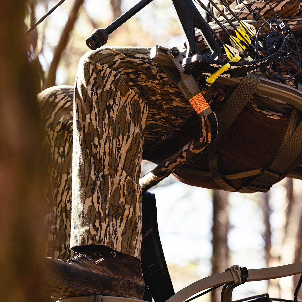 View of a man sitting in the Summit Dual Threat PRO SD climbing treestand in the Bow Hunting Position. The adjustable front bar is positioned underneath the seat, allowing for an open front.