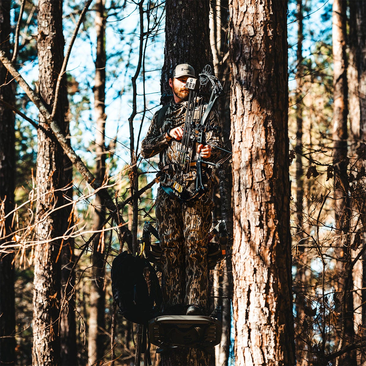 View of a man standing in the Summit Dual Threat PRO SD climbing treestand in the Bow Hunting Position. He is drawing his bow while standing up.