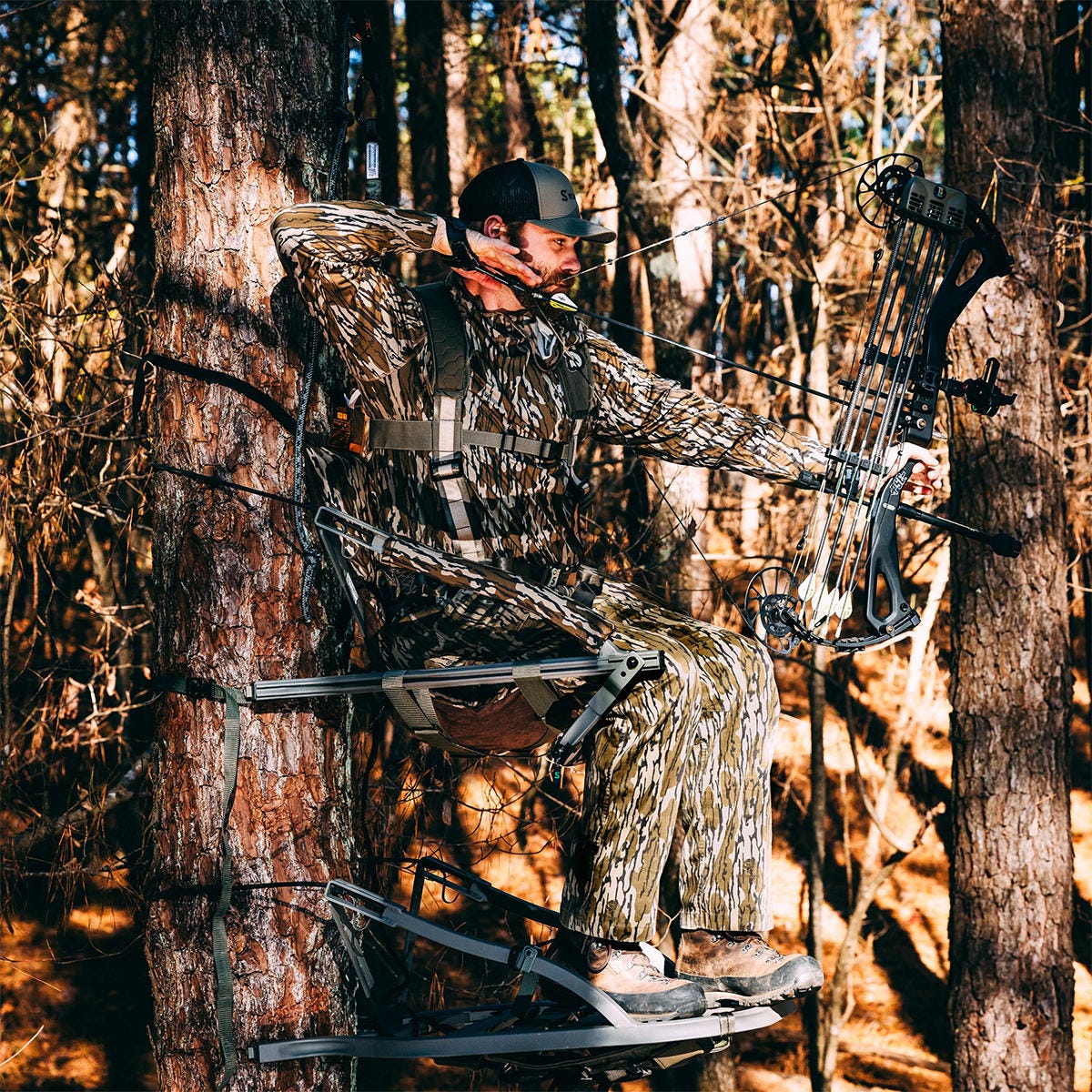 View of a man sitting in the Summit Dual Threat PRO SD climbing treestand in the Bow Hunting Position. He is drawing his bow while staying seated.