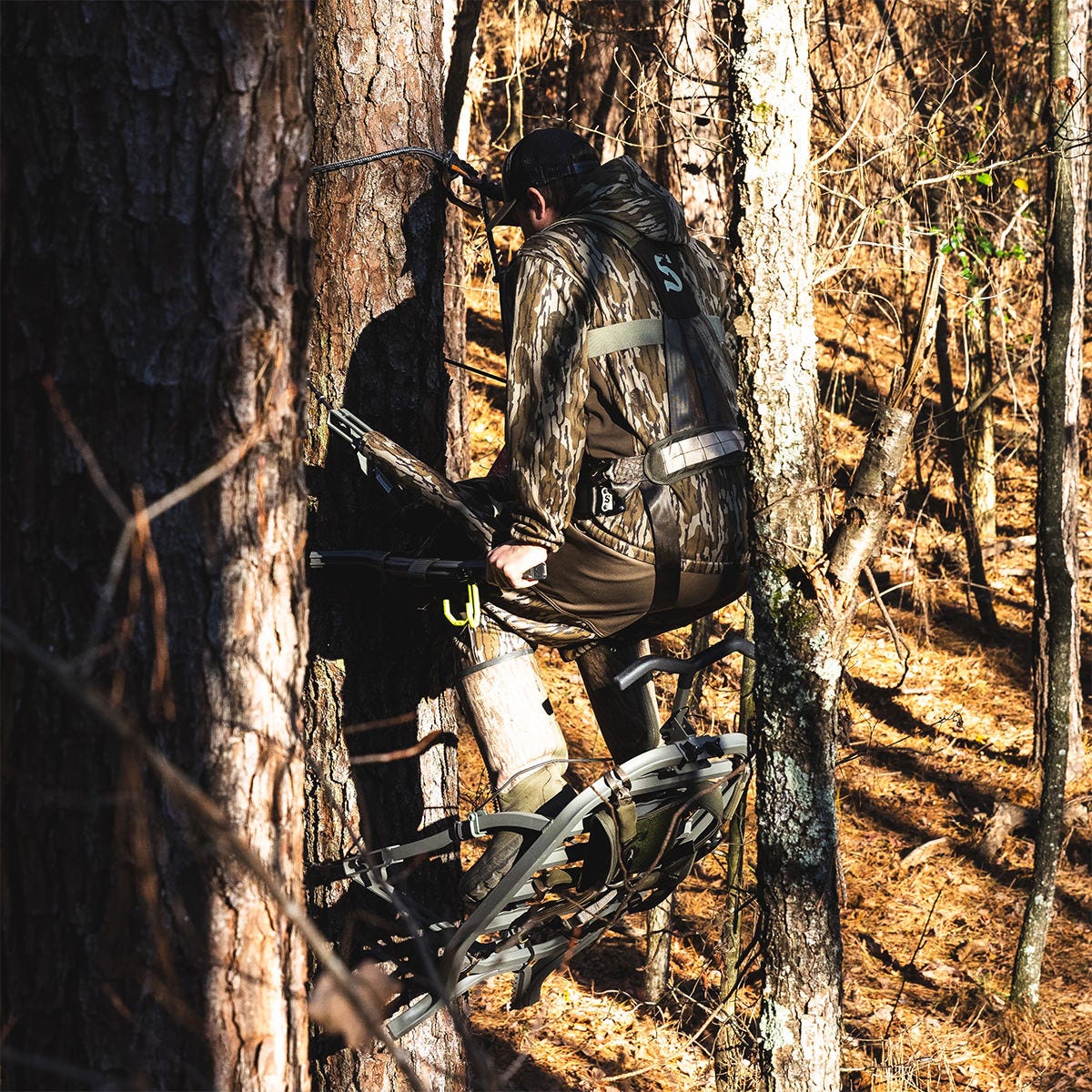 Full view of a man in camo ascending a tree using the Summit Dual Threat PRO SD climbing treestand in Hand Climber mode. The adjustable front bar has been removed.